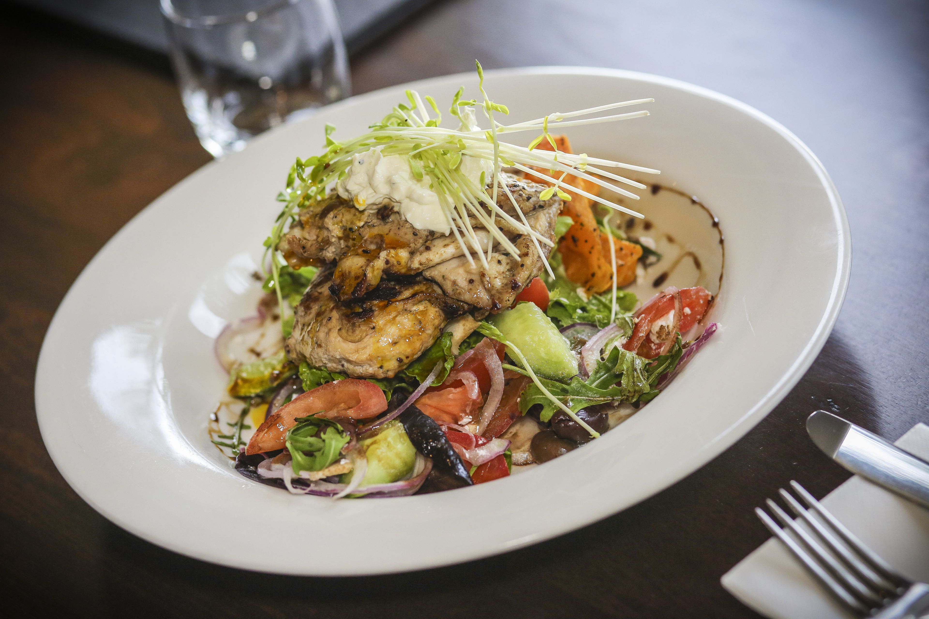 A plate of food with grilled chicken, vegetables, and a creamy sauce.