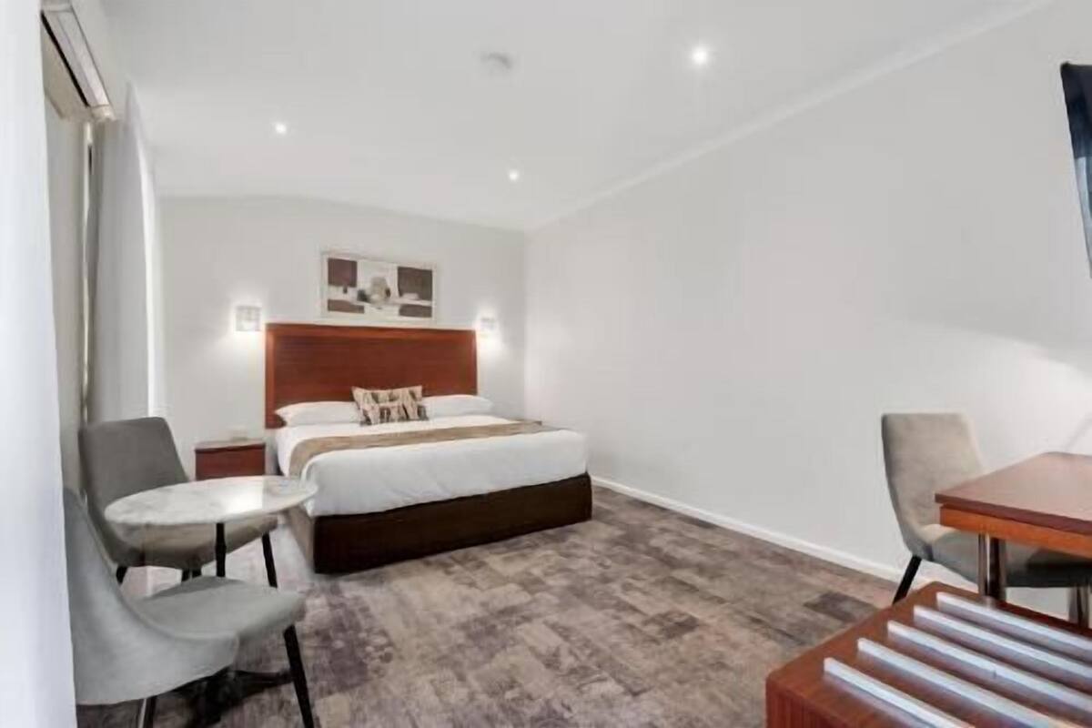 A hotel room with a bed, two chairs, a small table, and a wooden bench.