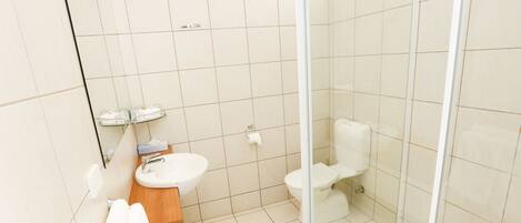 Un baño moderno con ducha envuelta en vidrio, tocador de madera y lavamanos blanco.