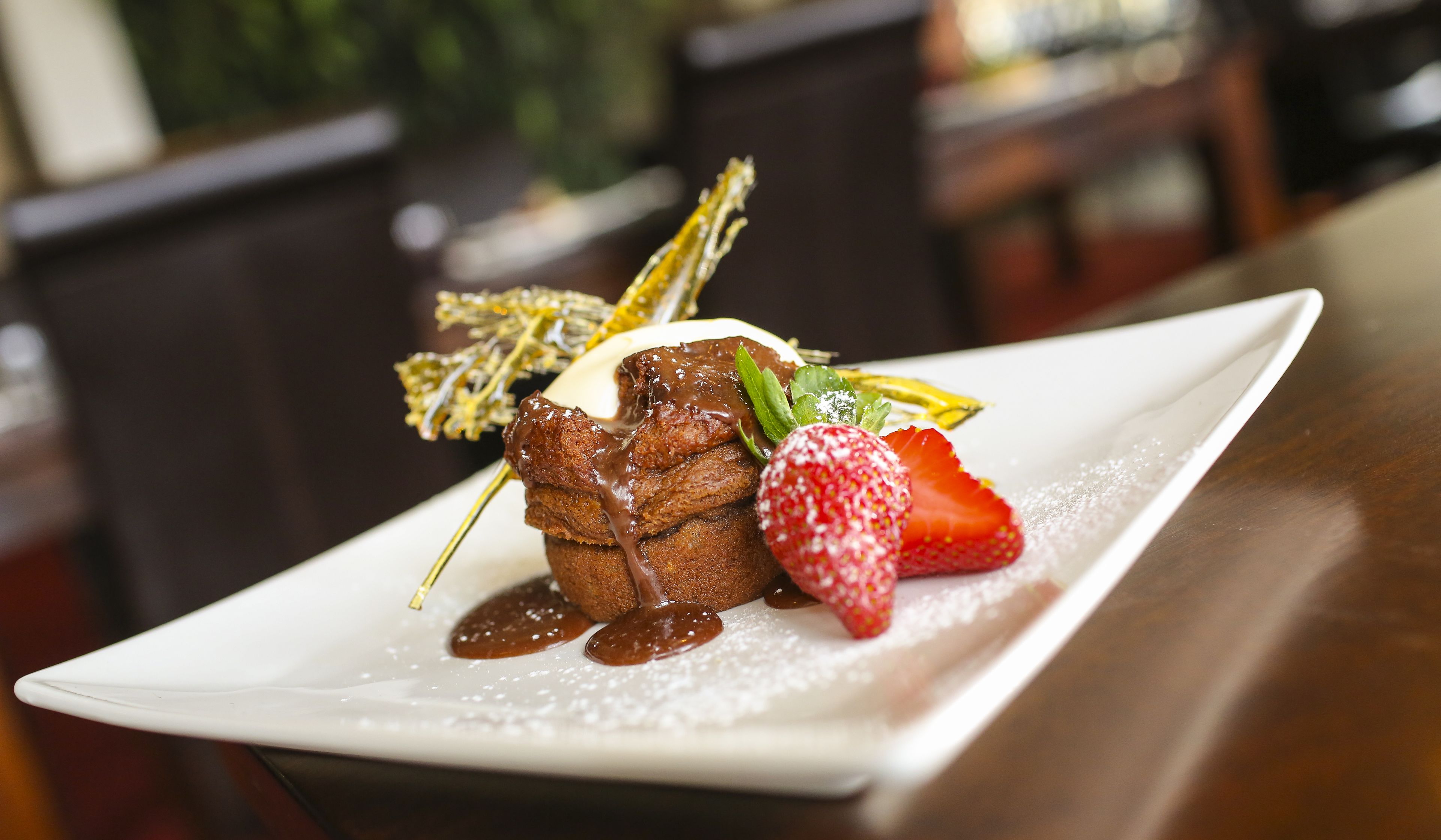 A dessert plate with a chocolate dessert, a strawberry, and a mint leaf garnish.