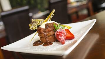 A dessert plate with a chocolate dessert, a strawberry, and a mint leaf garnish.