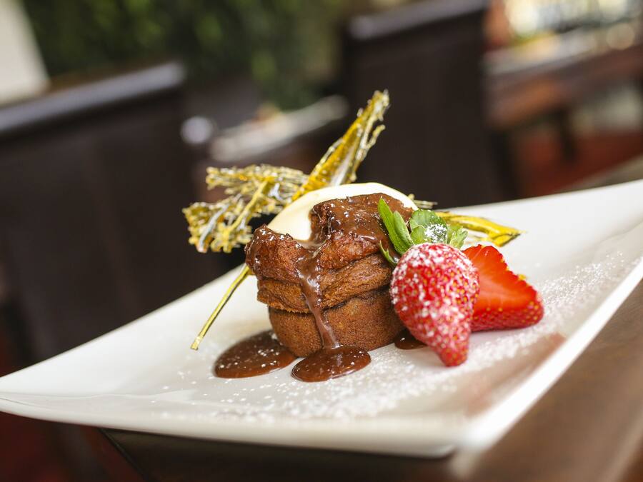 Un plato con un postre de chocolate, una fresa y una hoja de menta como decoración.