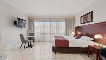 Una habitación de hotel con cama, mesita de noche, lámpara, televisor, silla y una pequeña mesa.