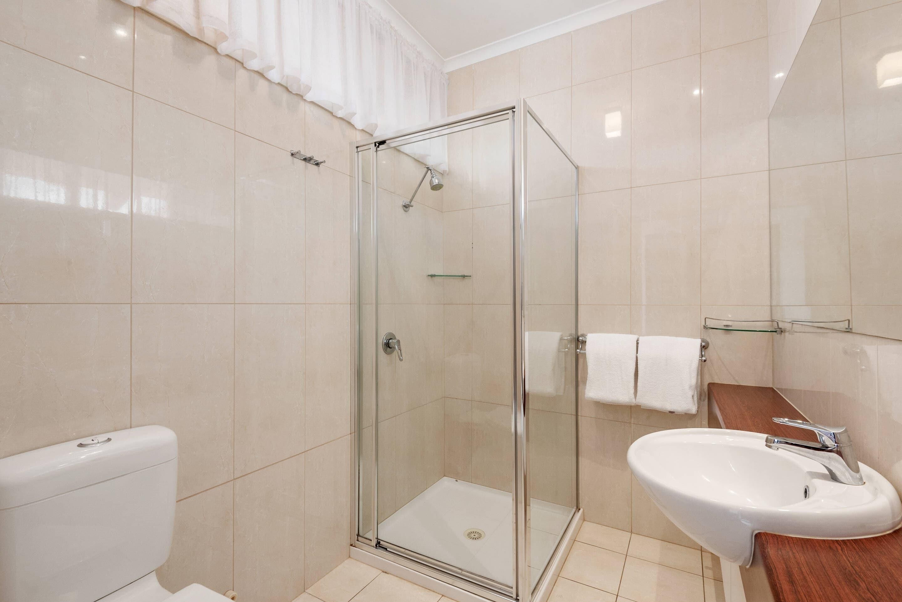 Un bagno moderno con doccia vetrata, un water bianco e un lavabo con piano in legno.
