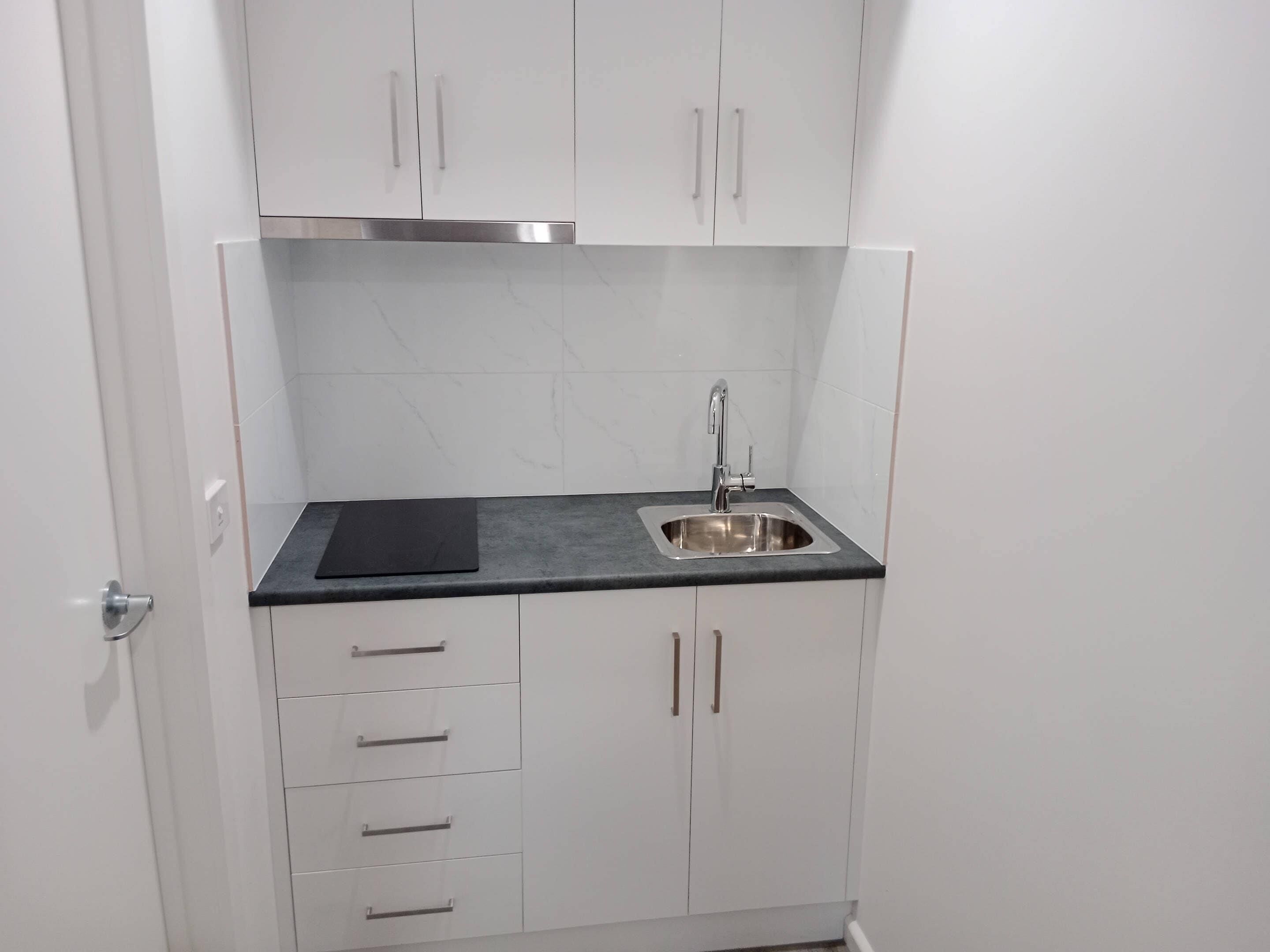 Een kleine keuken met witte kastjes, een RVS spoelbak en een zwart aanrecht.