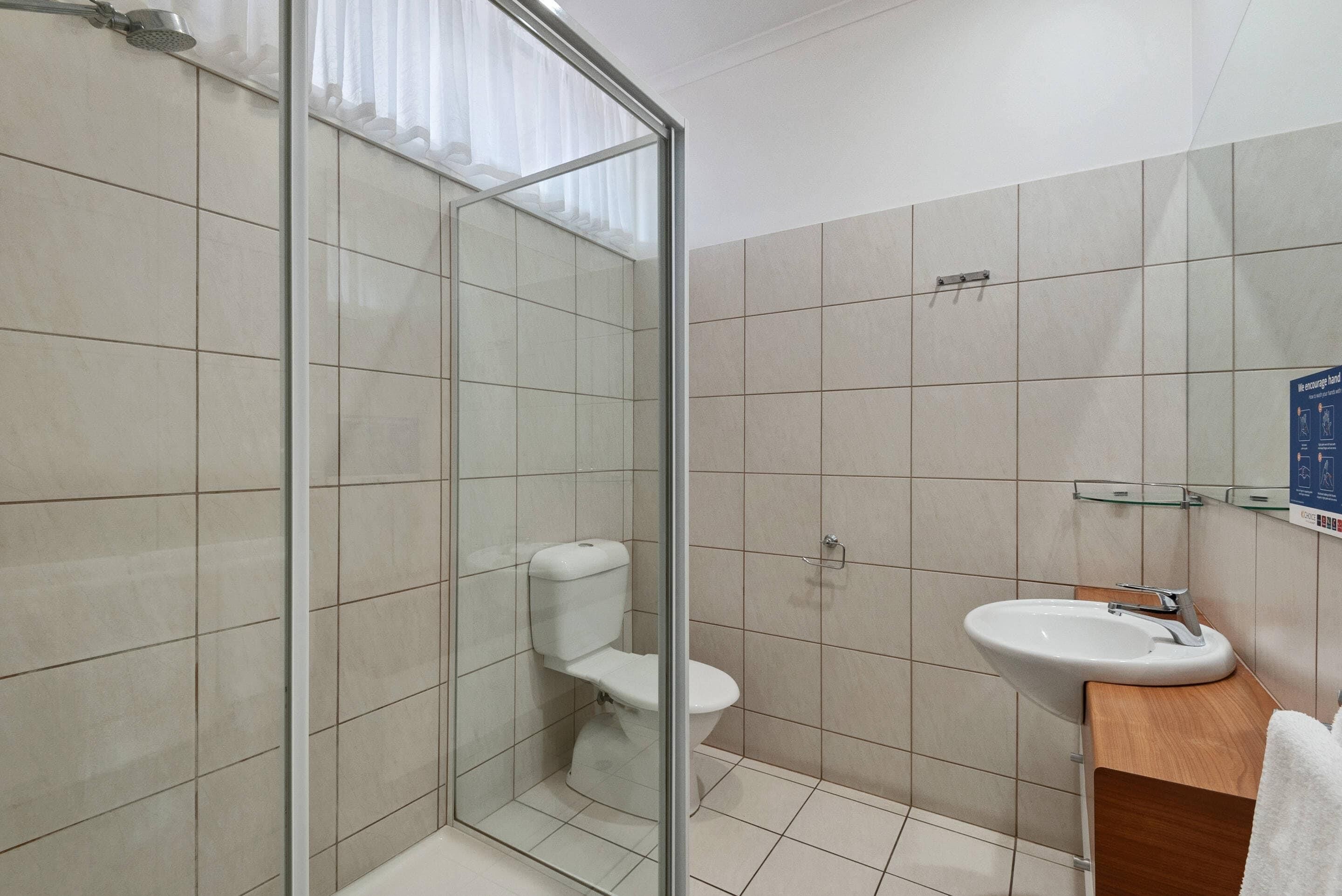A modern bathroom with a glass shower enclosure, a white toilet, and a sink with a wooden countertop.
