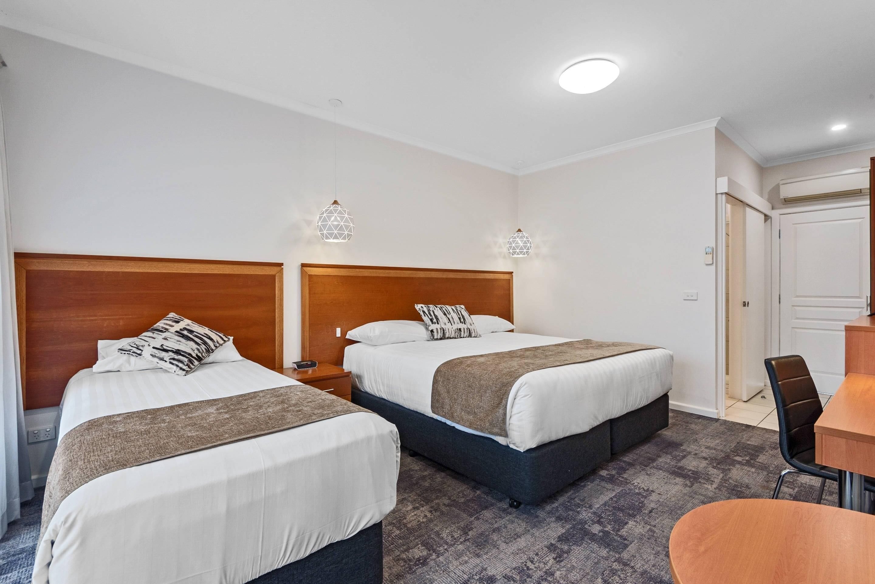 A hotel room with two beds, a wooden headboard, a small table, and a chair.