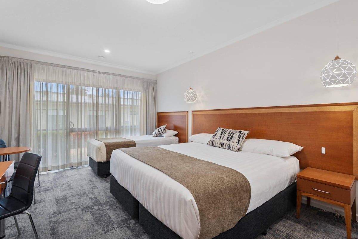 A hotel room with two beds, a desk, and a chair.
