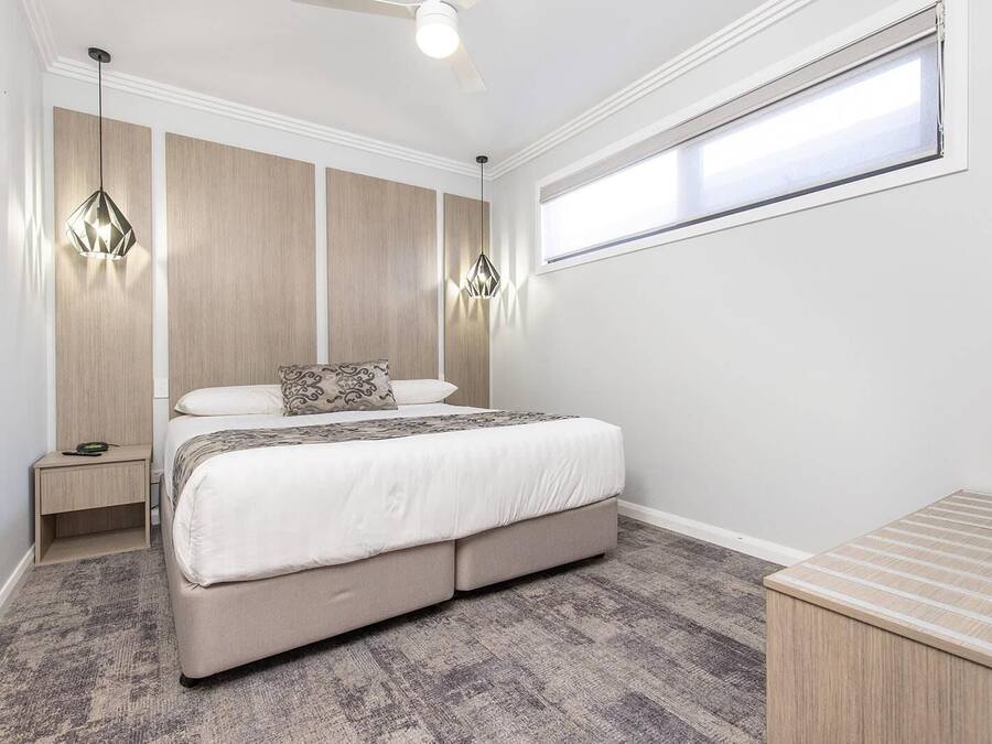 Un dormitorio con cama, mesitas de noche, ventilador de techo y ventana.