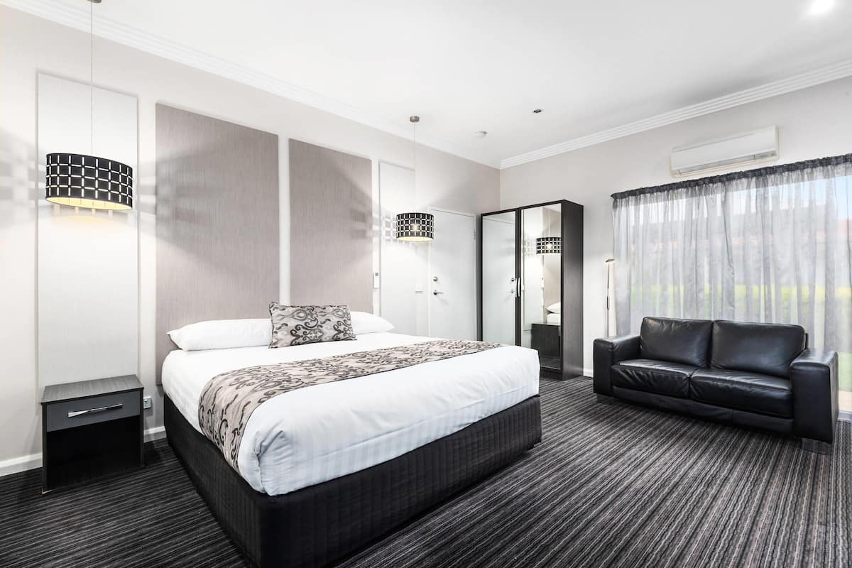 A modern hotel room with a large bed, a black leather sofa, and a walk-in closet.