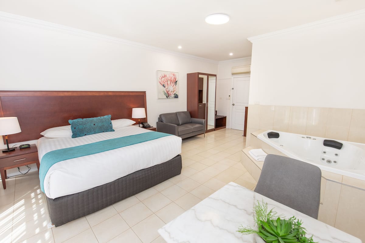 A hotel room with a large bed, a sofa, a desk with a chair, a bathroom with a bathtub, and a painting on the wall.
