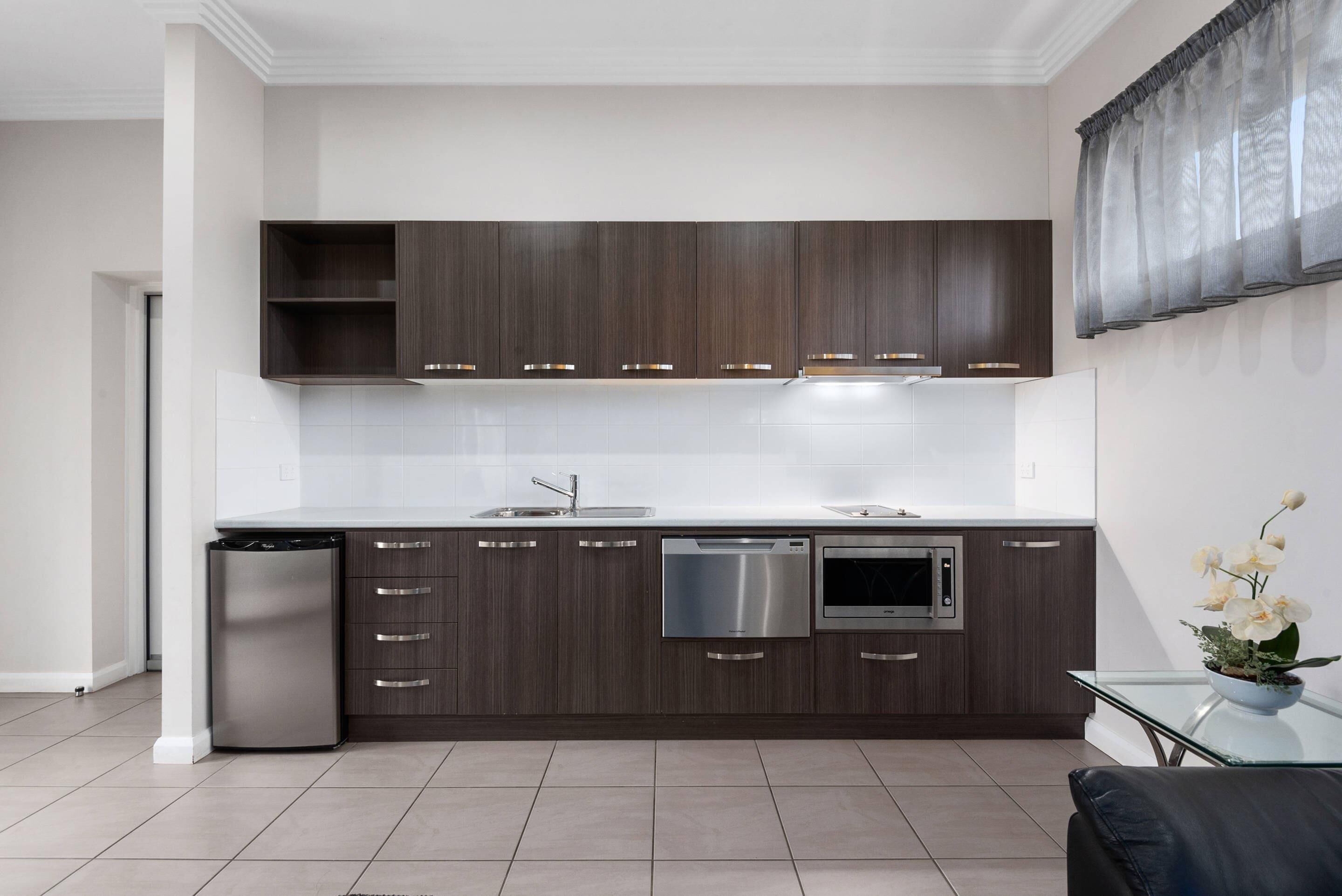 Una cocina moderna con armarios de madera oscura, electrodomésticos de acero inoxidable y una mesa de centro de vidrio con un arreglo floral.