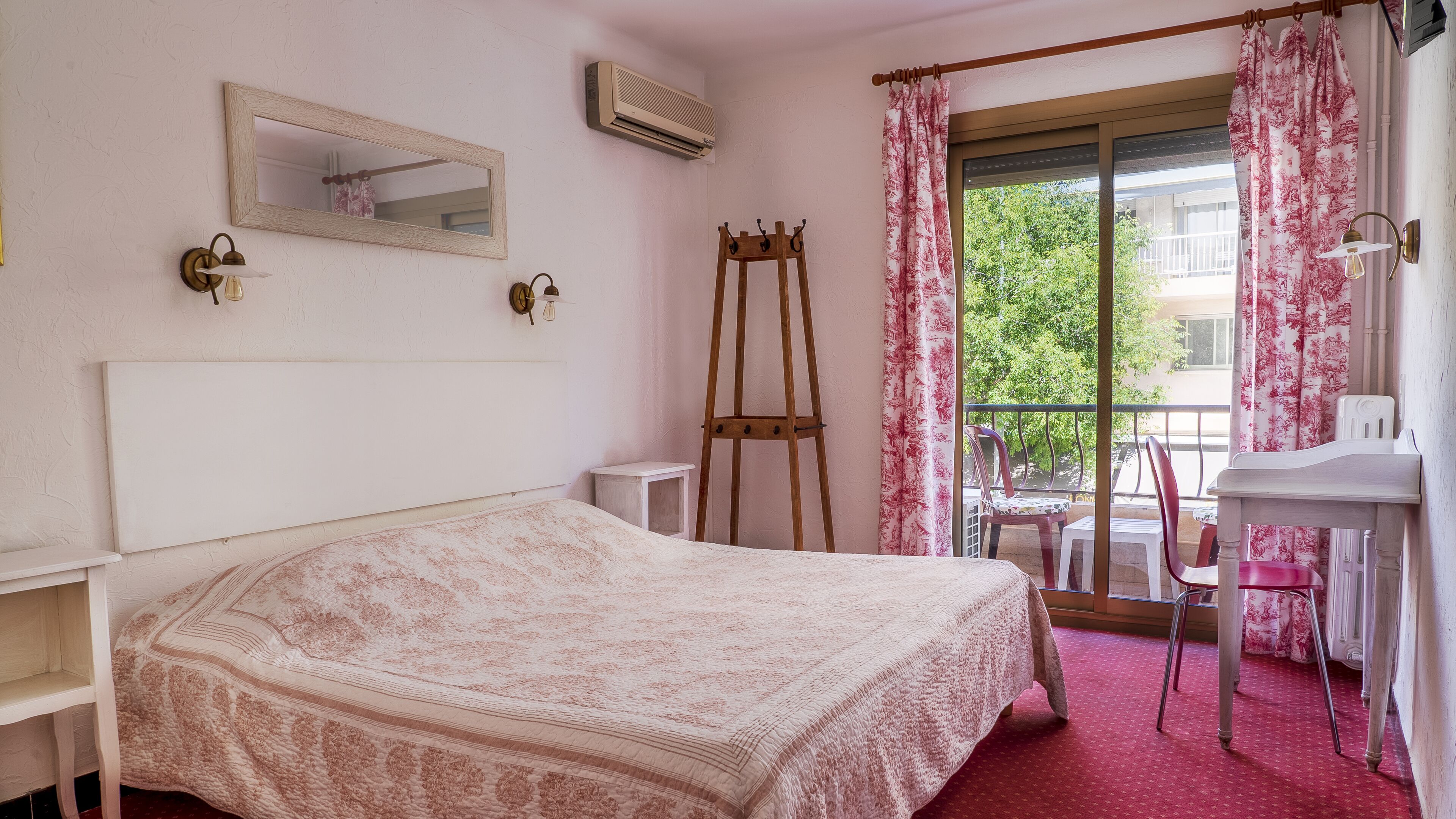 A bedroom with a bed, a small table, a chair, a ladder, a mirror, and a window with curtains.
