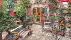 Un patio jardín con suelo de piedra, bancos de madera y plantas en macetas.