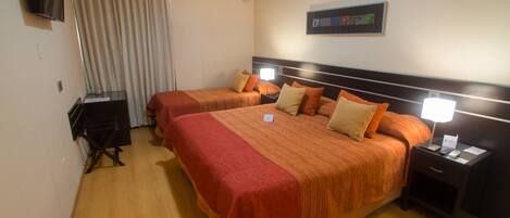 A hotel room with two beds, a TV, a desk, and a nightstand with a lamp.