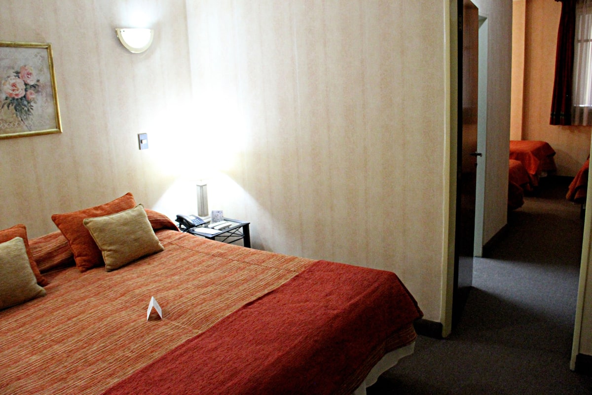 A hotel room with a bed, a nightstand, a lamp, and a painting on the wall.