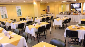 Un salón de conferencias con mesas dispuestas para una reunión, una zona de bufé y una pantalla de televisión mostrando un programa.