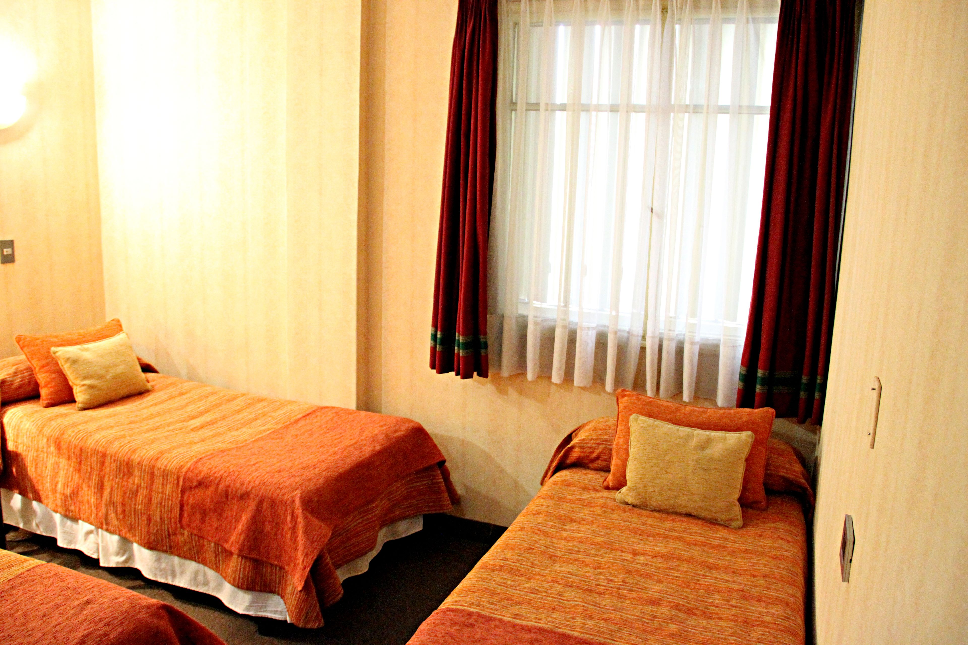Quarto de hotel com duas camas, cada uma com roupa de cama laranja e travesseiro bege.