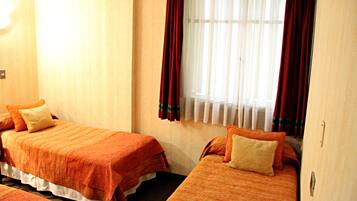Quarto de hotel com duas camas, cada uma com roupa de cama laranja e travesseiro bege.