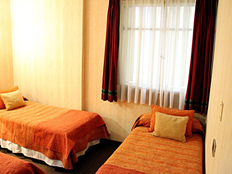 Quarto de hotel com duas camas, cada uma com roupa de cama laranja e travesseiro bege.