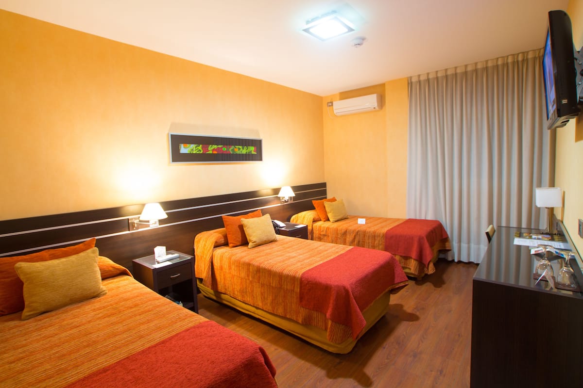 A hotel room with three beds, a desk, a television, and a wall-mounted air conditioner.