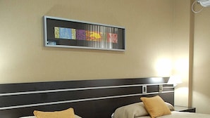 Habitación de hotel con dos camas, cabecero, una obra de arte colgada en la pared y una mesita de noche con lámpara.