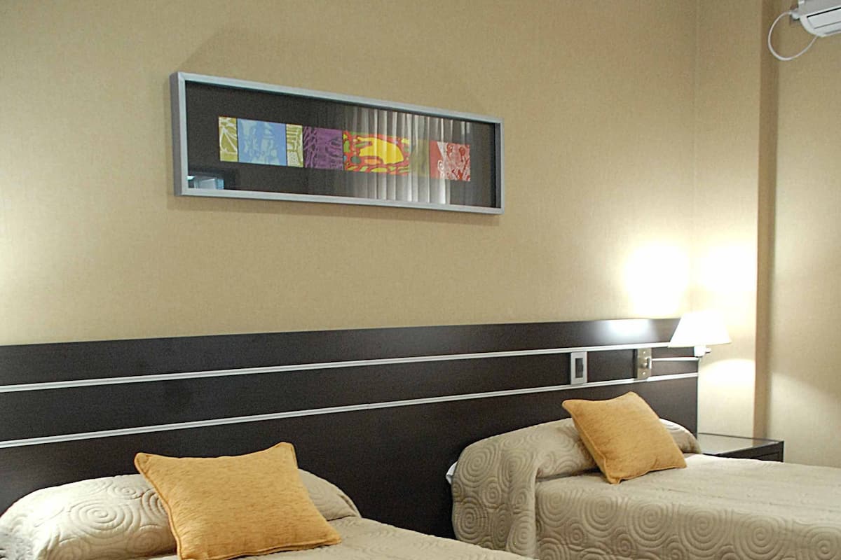 A hotel room with two beds, a headboard, a wall-mounted artwork, and a nightstand with a lamp.