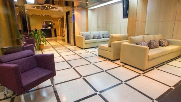 Un vestíbulo de hotel con un mostrador de recepción, dos sofás, un sillón púrpura y piso de baldosas.