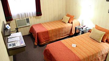 Une chambre d’hôtel avec deux lits, un bureau avec une chaise, une lampe et une fenêtre avec des rideaux.