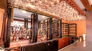 Zona de bar con estantes llenos de botellas de licor, un espejo y una lámpara de araña.