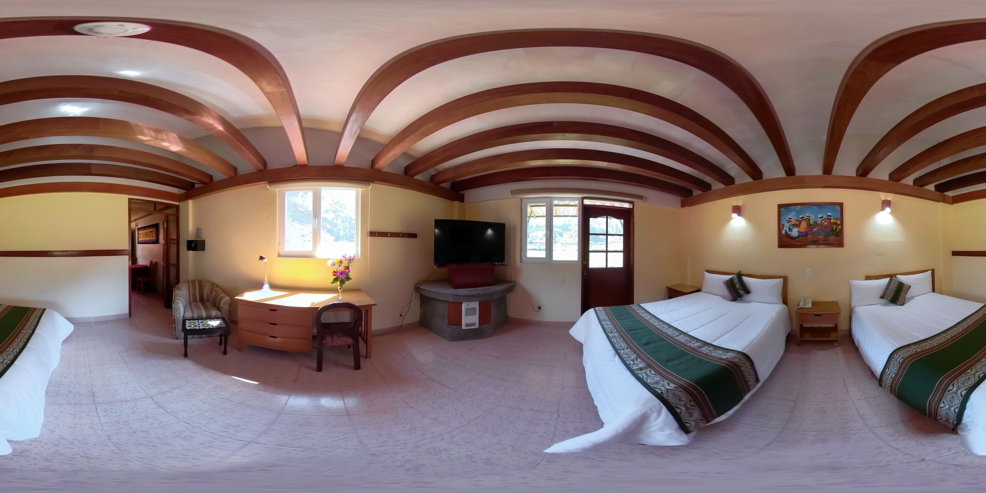 Quarto de hotel com teto abobadado, duas camas com roupa de cama verde e branca, uma escrivaninha com cadeira, uma televisão e um quadro na parede.