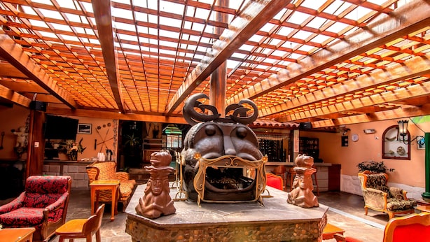 Un interior acogedor con chimenea de piedra, mobiliario de madera y un alto techo de madera con un diseño de cuadrícula.
