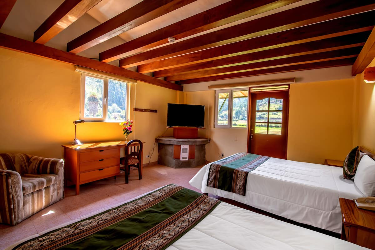 Une chambre avec deux lits, un bureau, une chaise, une télévision et une fenêtre donnant sur un paysage verdoyant.