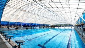 Una piscina interior con varias pistas, techo alto y cubierta azulada.