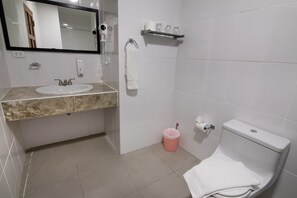 Un baño con lavamanos, espejo, inodoro y un bote de basura.