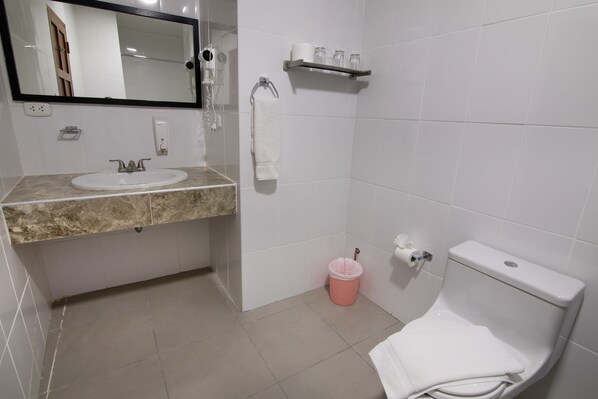 A bathroom with a sink, mirror, toilet, and a trash bin.