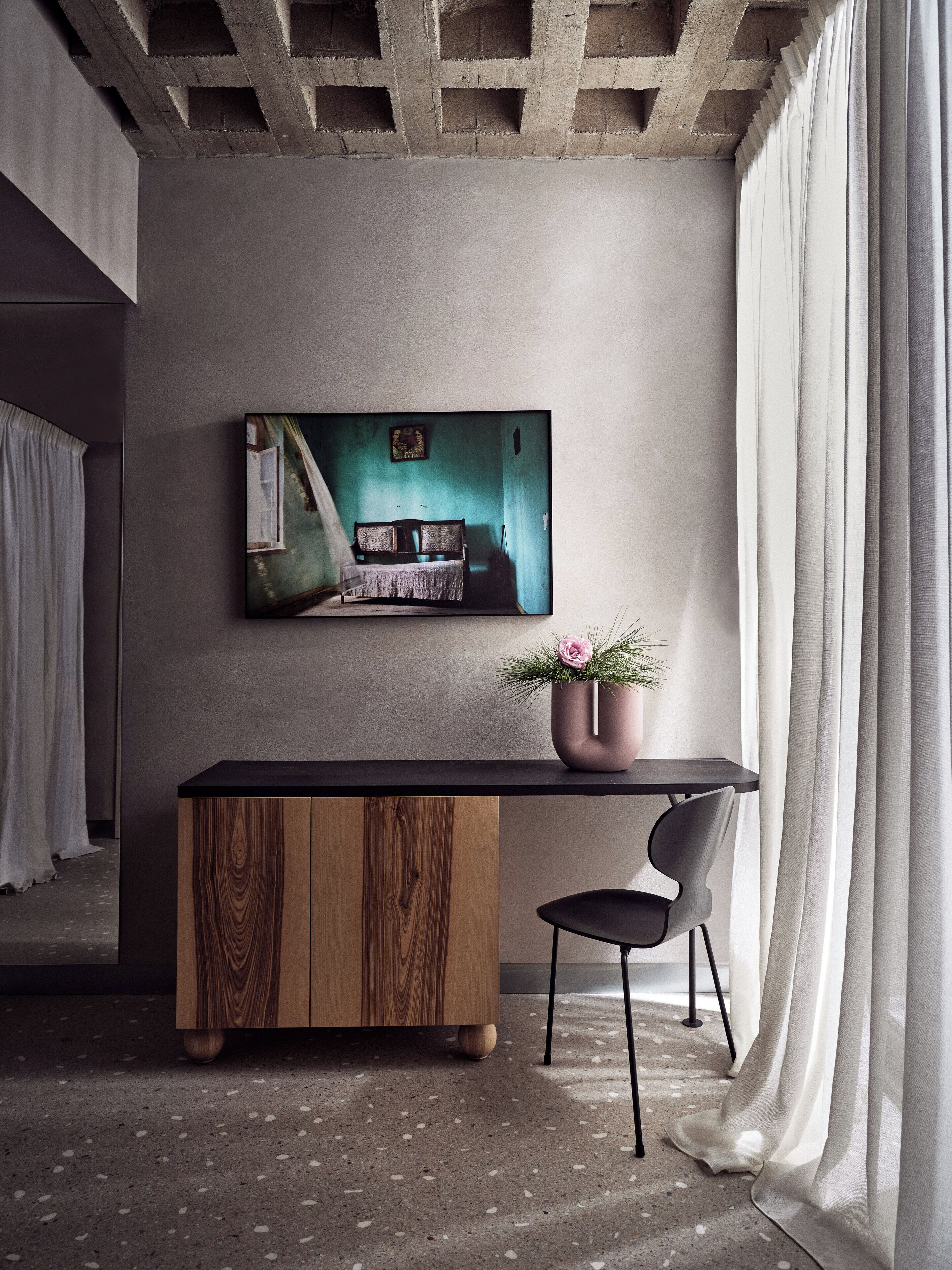 A modern room with a wooden cabinet, a black chair, and a painting on the wall.