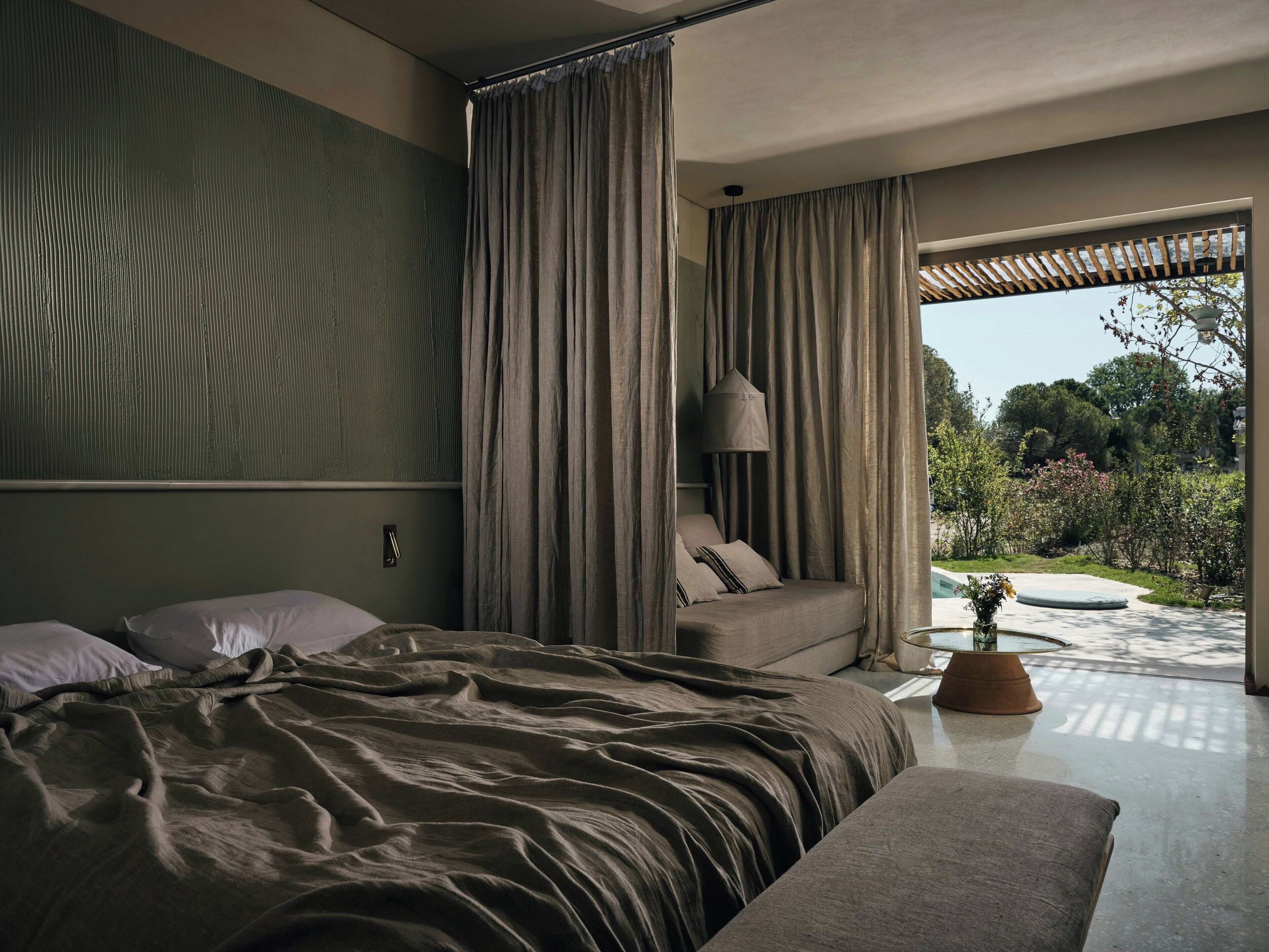 A bedroom with a bed, curtains, a bedside table, and a view of the garden.