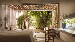 A modern bedroom with a large bed, a seating area with a chair, a small table, and a potted plant. - Ekies All Senses Resort, a Member of Design Hotels (Sithonia)