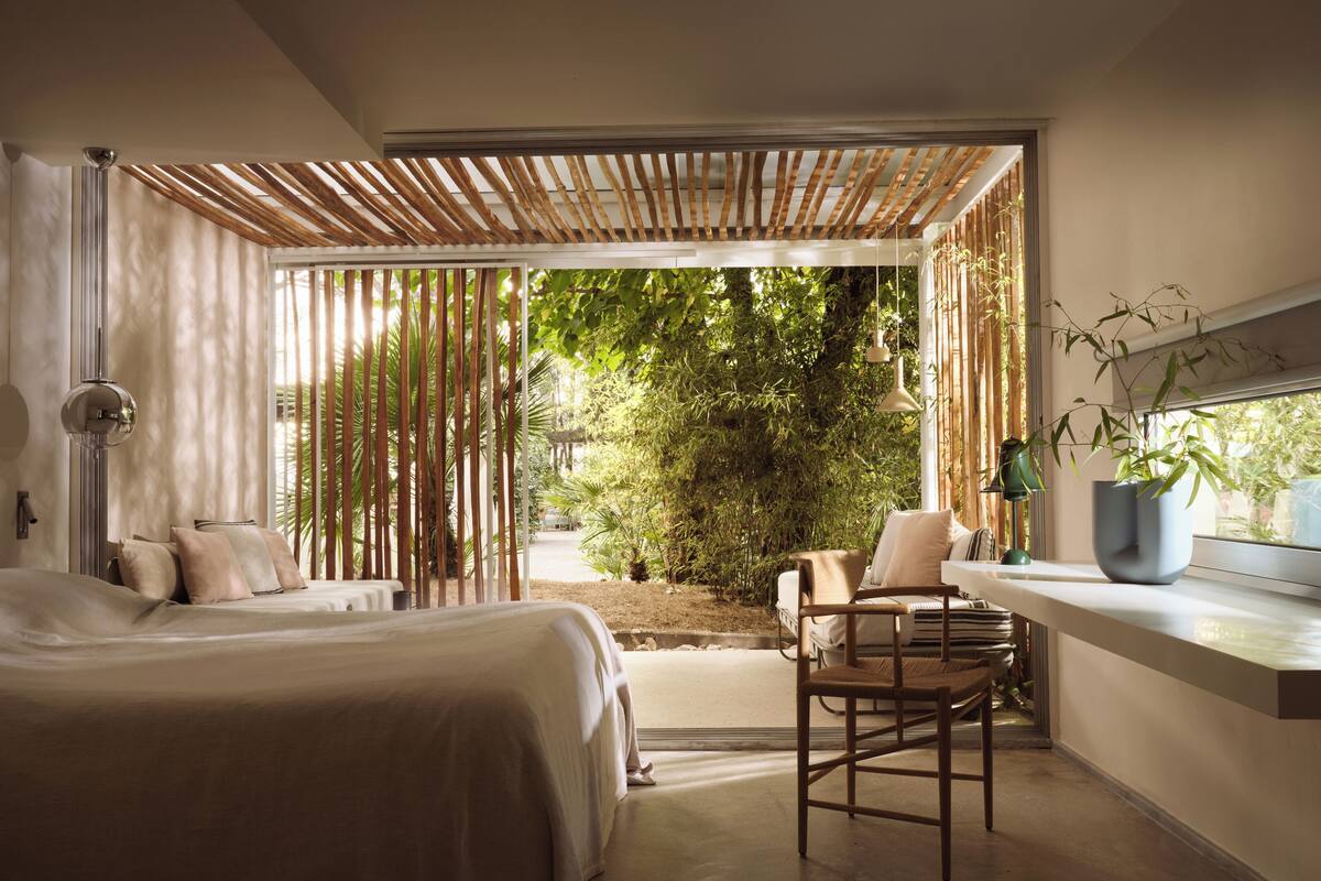 A modern bedroom with a large bed, a seating area with a chair, a small table, and a potted plant.