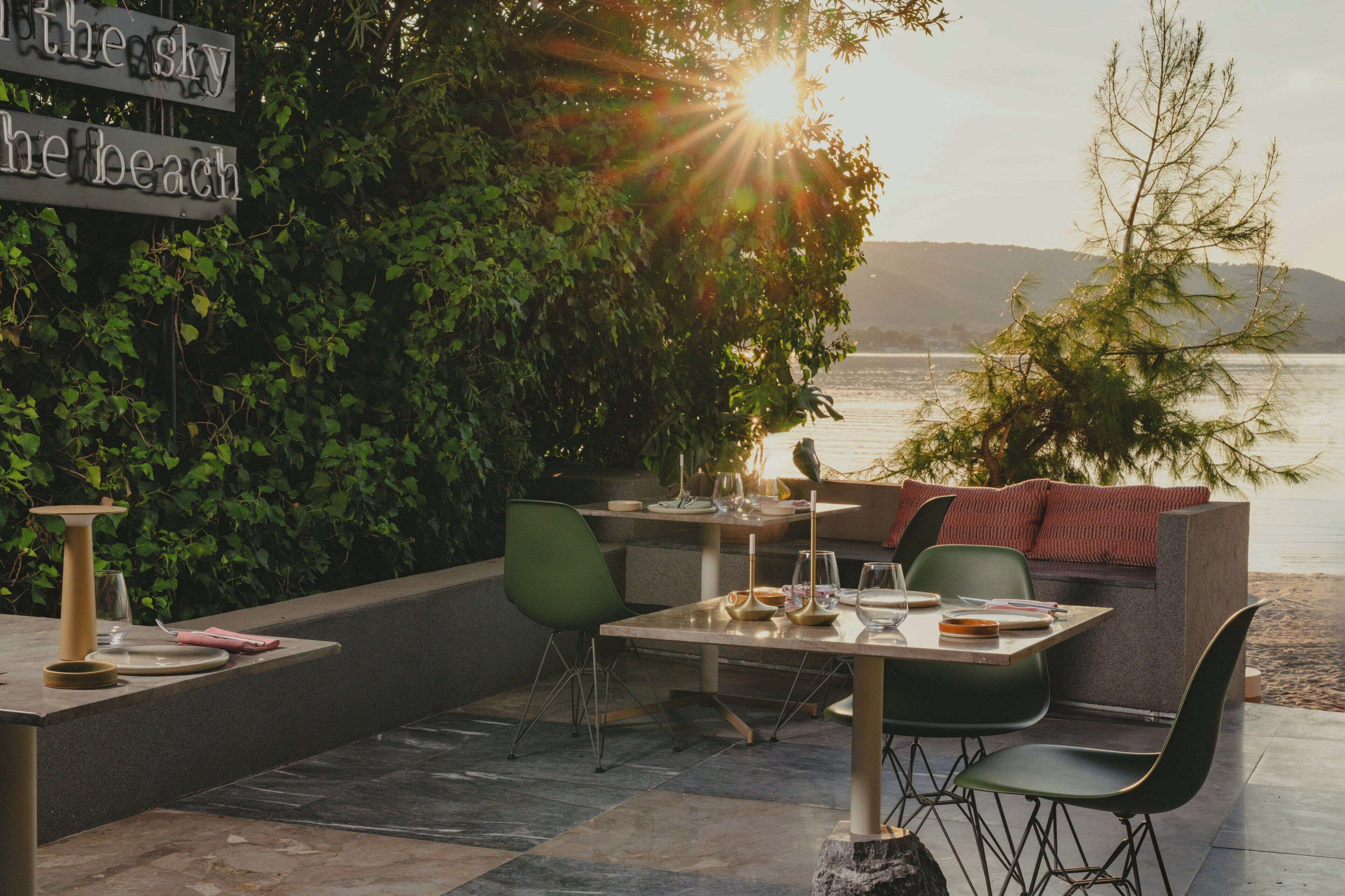 An outdoor seating area with a view of the water, a sign reading 'the sky the beach,' and a table set for dining.