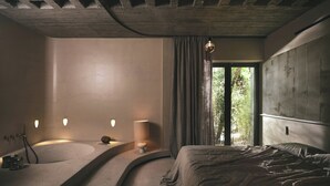 A modern bedroom with a curved bathtub, a large bed, and a window with curtains. - Ekies All Senses Resort, a Member of Design Hotels (Sithonia)