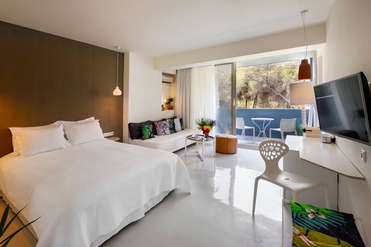 A modern hotel room with a large bed, a sofa, a TV, and a balcony with a view.