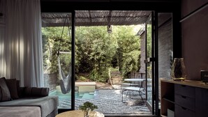 A modern living room with a sofa, a round coffee table, and a glass door leading to a garden with a pool and outdoor furniture. - Ekies All Senses Resort, a Member of Design Hotels (Sithonia)