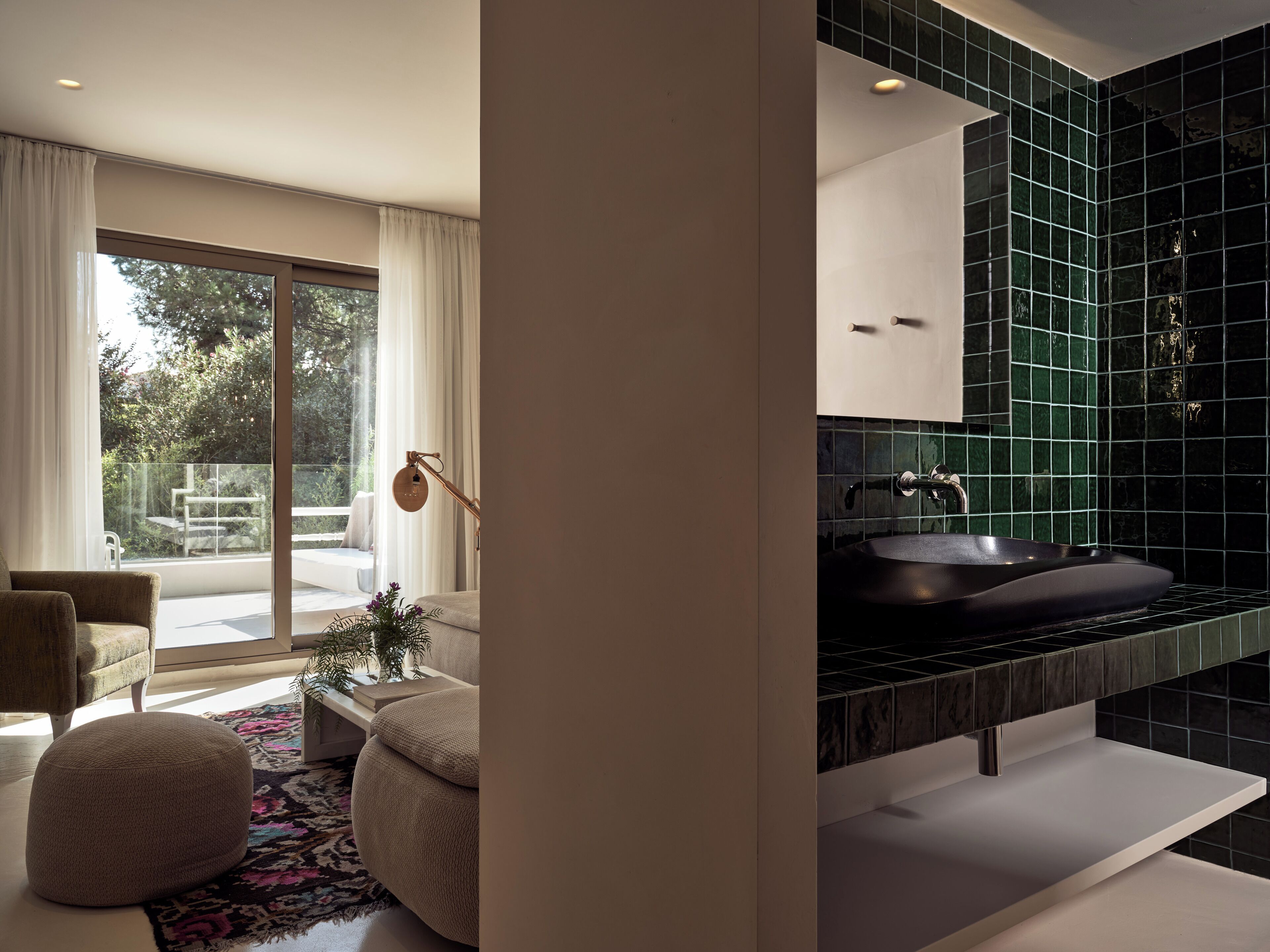 A modern bathroom with a black sink, green tiles, and a large window.
