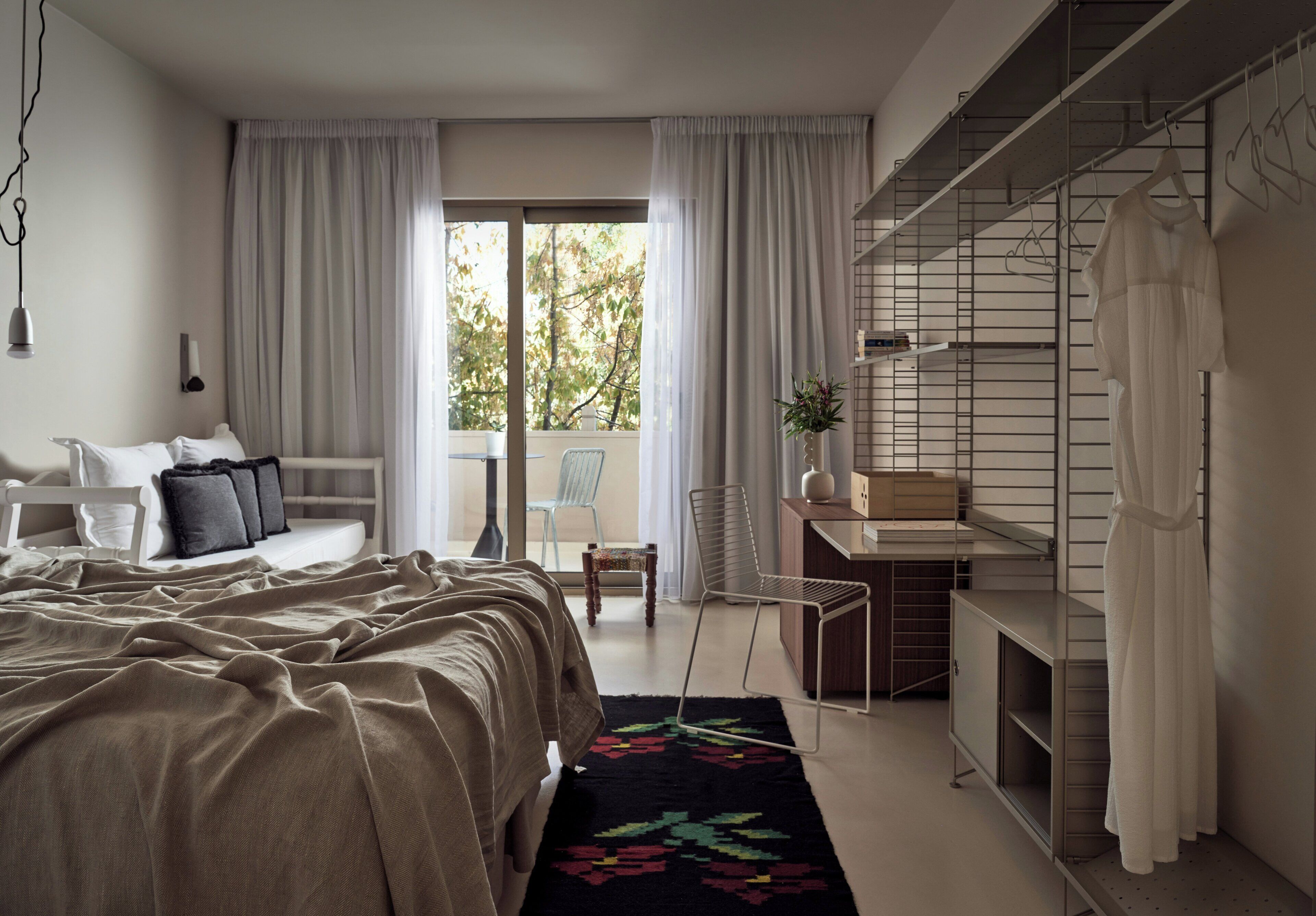 Une chambre à coucher comprenant un lit, un bureau, une chaise, une armoire et donnant sur l’extérieur.