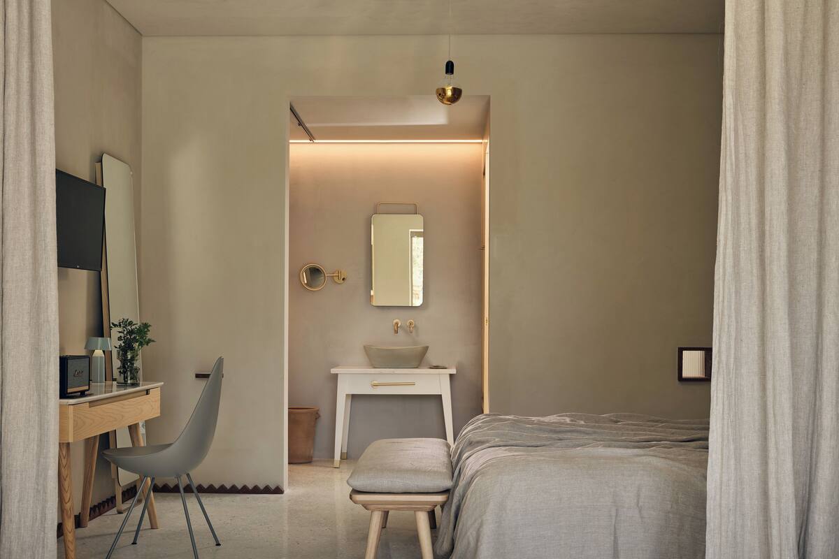 A bedroom with a bed, bedside table, chair, desk, mirror, and a small window.