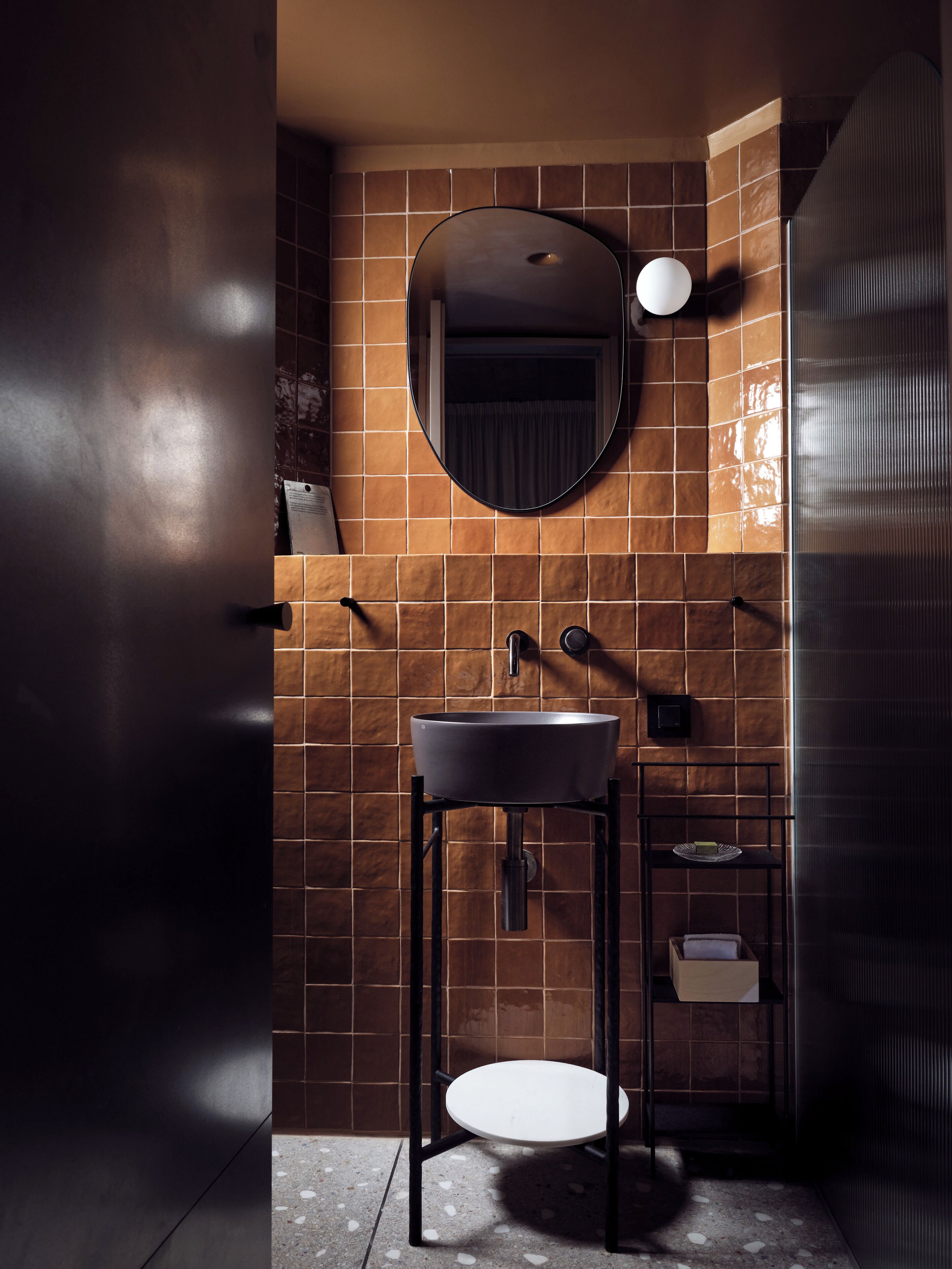 A modern bathroom with a round mirror, a sink, and a shelf with toiletries.