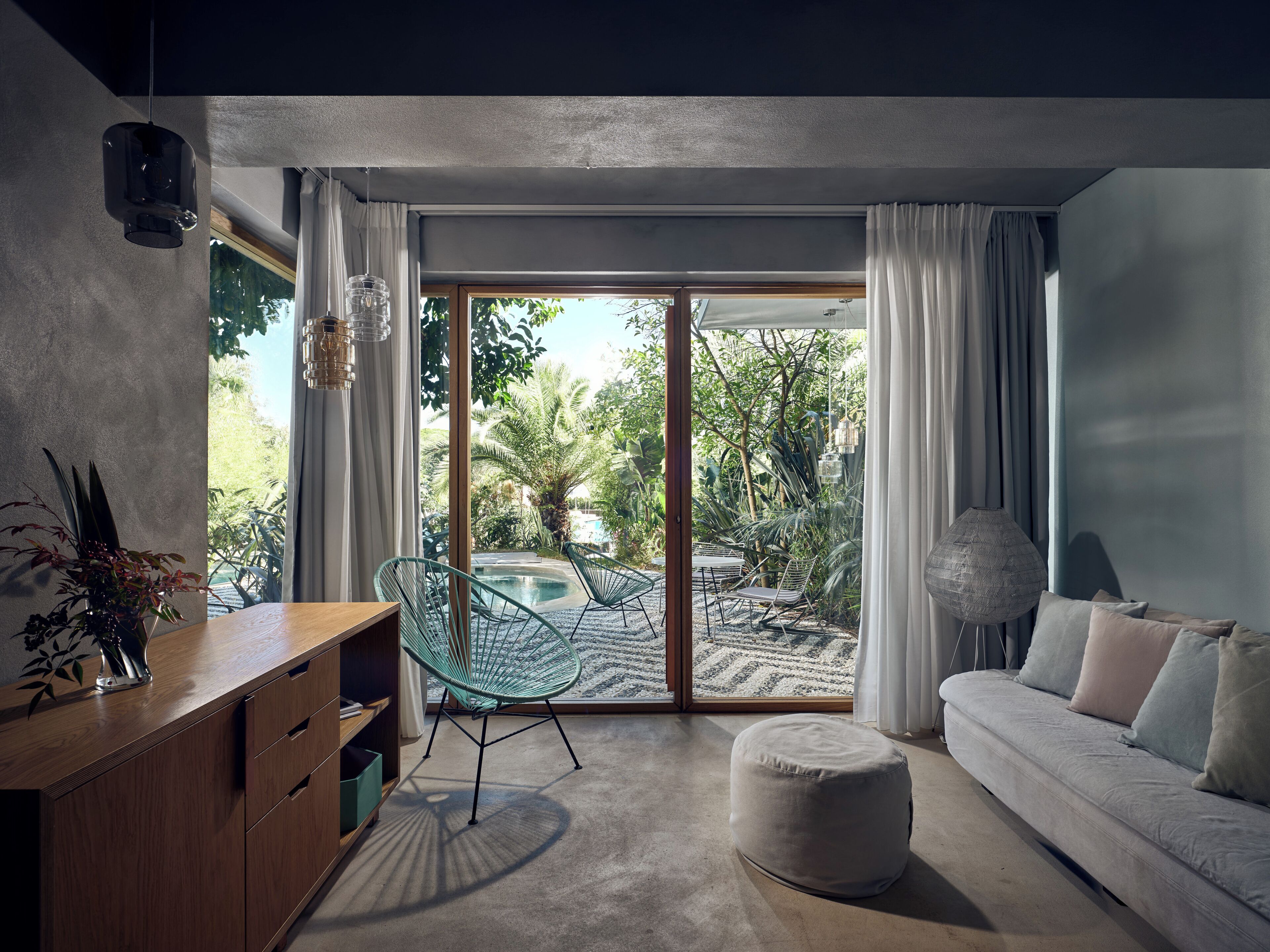 A modern living room with a glass door leading to a pool area, a wooden sideboard, and a sofa with cushions.