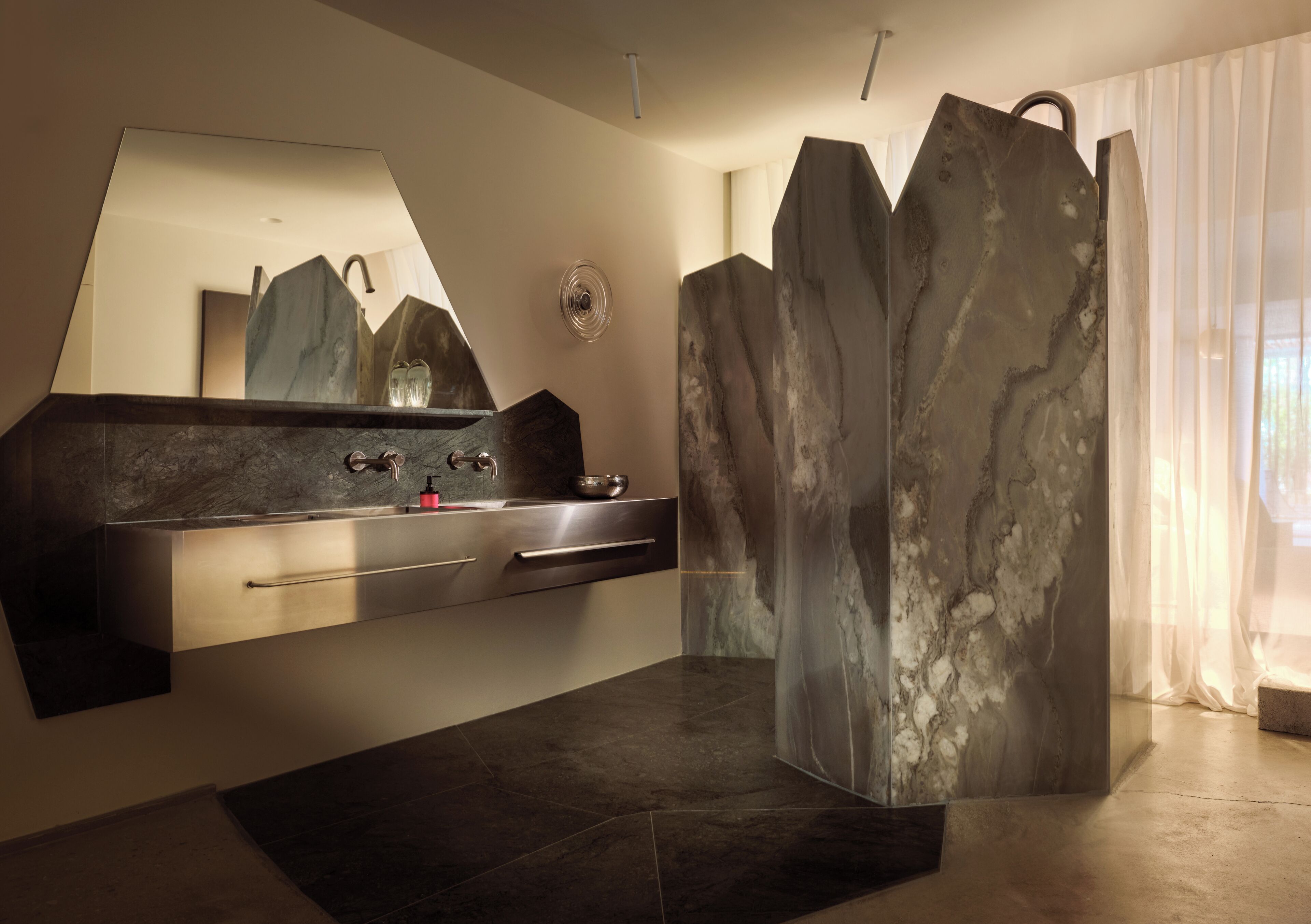 A modern bathroom with a large mirror, a marble sink, and a unique geometric partition.